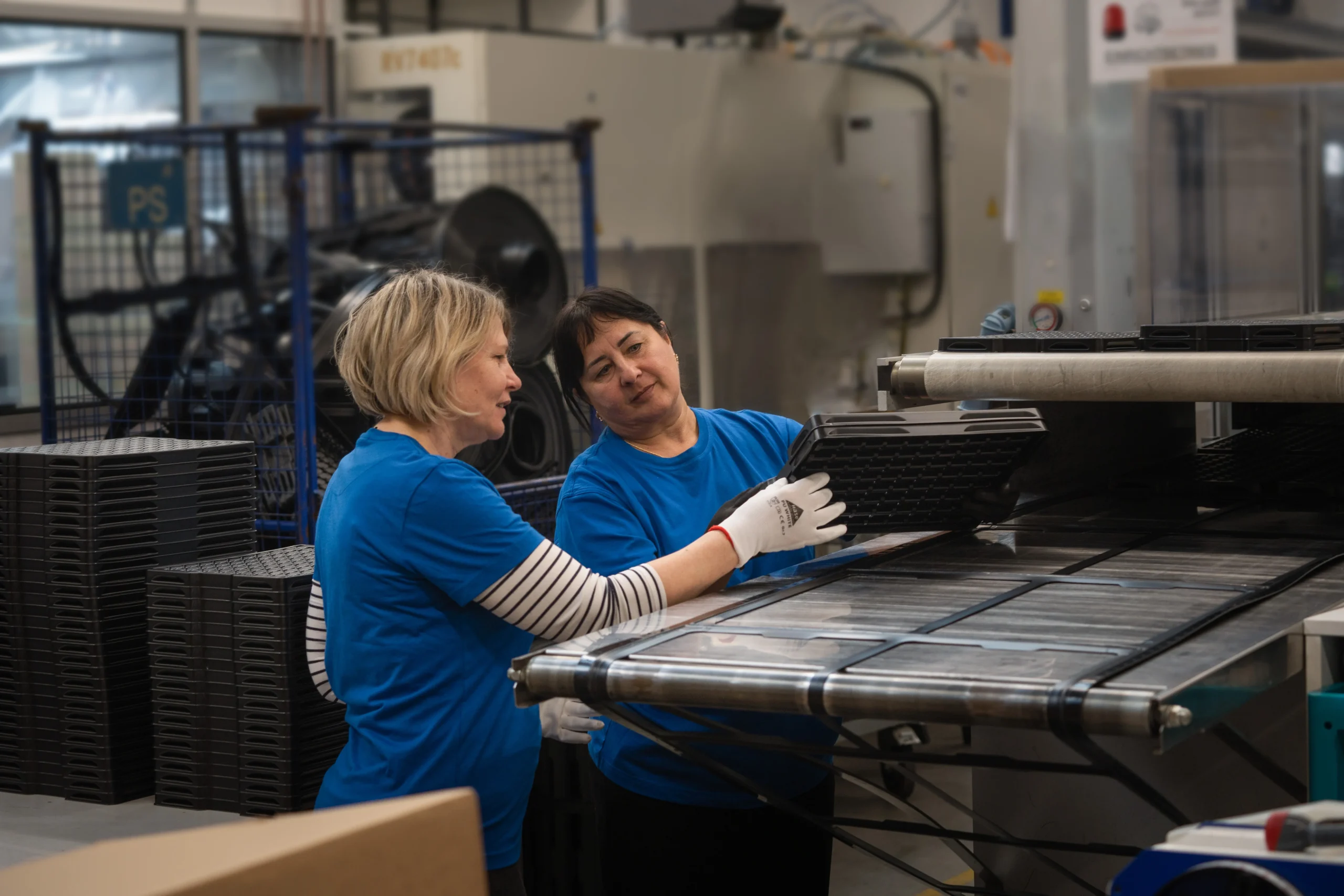 Zwei Mitarbeiterinnen von Benker prüfen gemeinsam ein frisch tiefgezogenes schwarzes Tray an der Produktionsanlage