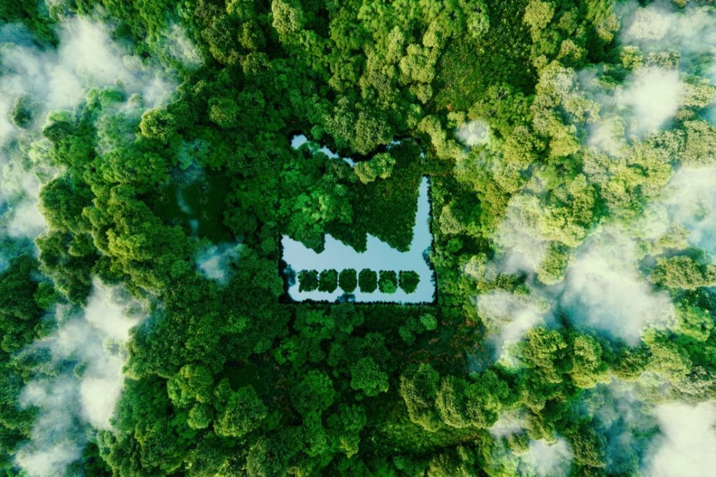 Luftaufnahme eines von Wald umgebenen Fabrikgeländes in Form eines stilisierten Fabriksymbols