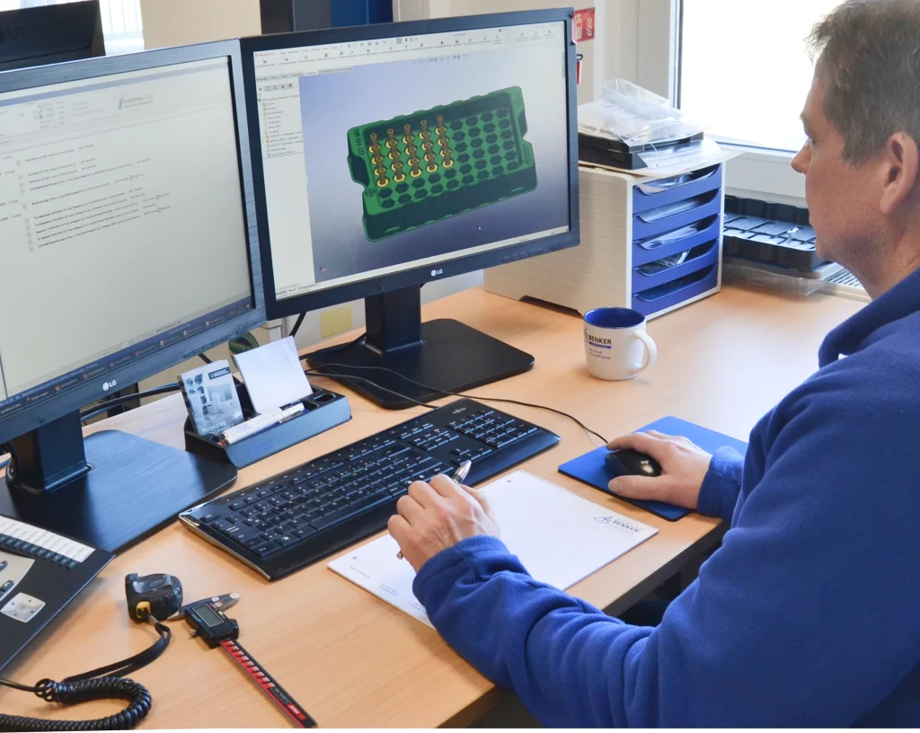 Konstrukteur von Benker am Zwei-Monitor-Arbeitsplatz, auf dem Bildschirm das 3D-Modell eines Trays mit Nestern